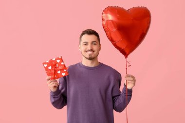Kalp şeklinde balonu ve pembe arka planda hediye kutusu olan yakışıklı bir adam.