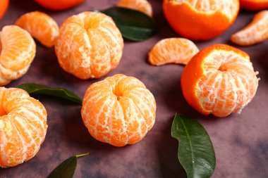 Mor arka planda yaprakları olan taze mandalinalar.