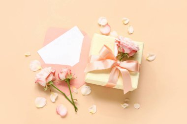 İçinde boş kart, hediye kutusu ve bej arka planda güller olan zarf.