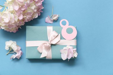 Hediye kutusu ve mavi arka planda ortanca çiçekleri olan kağıttan yapılmış 8 figür. Uluslararası Kadınlar Günü