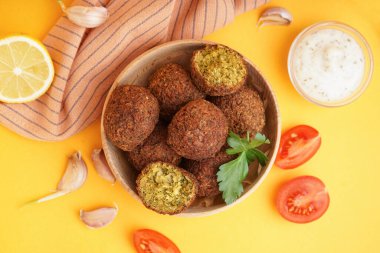 Nefis falafel köfteli ahşap kase, domates, sarımsak ve turuncu arka planda sos.
