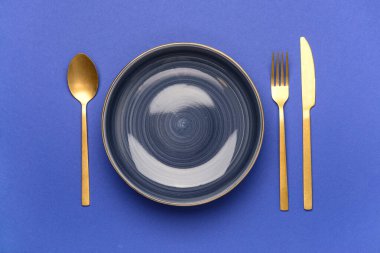 Mavi arka planda altın çatal bıçak takımı olan bir kase