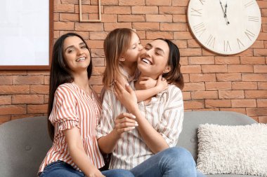 Evlatlık küçük kızı olan genç lezbiyen çift evdeki kanepede oturuyor.