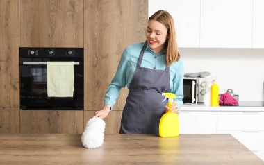Genç kadın mutfakta pp-tozster ile masayı temizliyor.