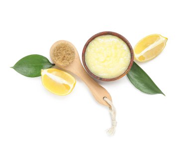 Bowl of lemon body scrub with massage brush isolated on white background