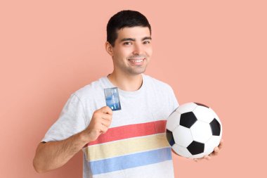 Futbol topu ve pembe arka planda kredi kartı olan mutlu genç bir adam. Spor bahsi konsepti