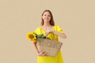 Bej arka planda güzel ayçiçekleri olan hasır çanta tutan kadın.