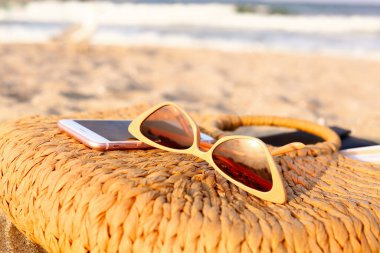 Saman çantalı şık güneş gözlükleri ve deniz kıyısında telefon, yakın plan.