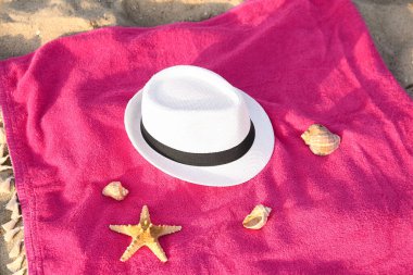 Şık hasır şapkalı renkli havlu ve kumdaki deniz kabukları.