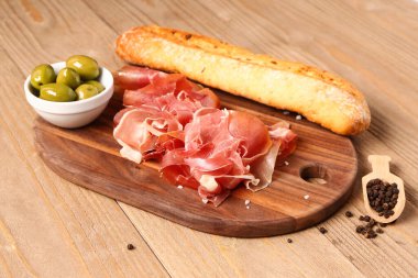 Lezzetli jambon, zeytin ve ekmek dilimleri ahşap arka planda.
