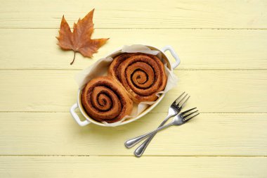 Lezzetli tarçınlı çörekler ve sarı ahşap arka planda sonbahar yaprağı pişirmek.