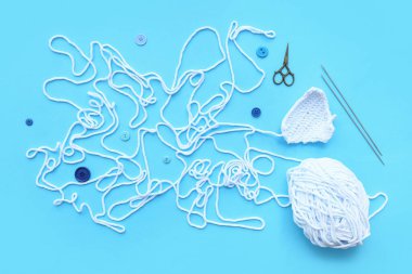 Mavi arka planda örgü iğneleri, iplik yumağı ve makas