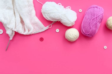 Örgü iğneleri, iplik topları ve pembe arka plandaki düğmeler.