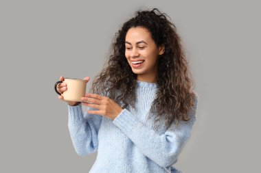 Gri arka planda sıcak şarap kadehiyle mutlu genç Afro-Amerikalı kadın.