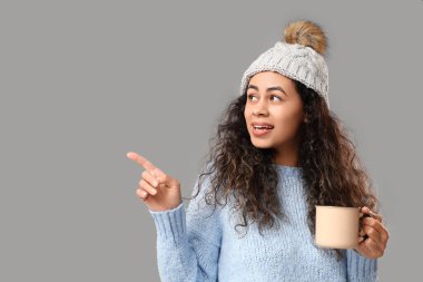 Güzel Afro-Amerikalı bir kadın, elinde sıcak şarapla gri arka plandaki bir şeyi işaret ediyor.