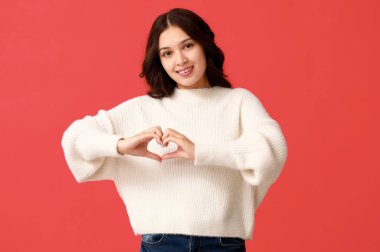 Güzel genç Asyalı kadın kırmızı arka planda kalp hareketi gösteriyor. Sevgililer Günü kutlaması