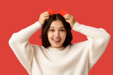 Renkli arka planda kırmızı kağıt kalpli mutlu bir Asyalı kadın. Sevgililer Günü kutlaması