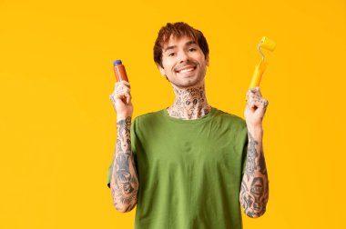 Sarı arka planda boya ve silindir şişesi olan mutlu genç bir adam.