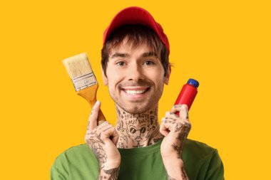 Sarı arka planda boya ve fırçayla mutlu genç adam, yakın plan.
