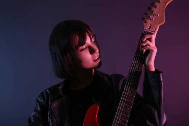 Koyu arka planda elektro gitar çalan havalı genç bir kadın.