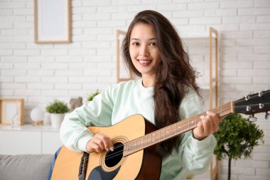 Evde gitar çalan genç ve güzel bir kadın.