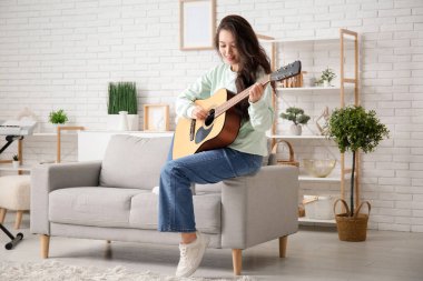 Evde gitar çalan genç ve güzel bir kadın.