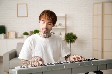 Evde sentezleyici çalan dövmeli genç adam.