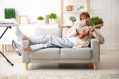 Havalı dövmeli genç adam evde ukulele çalıyor.