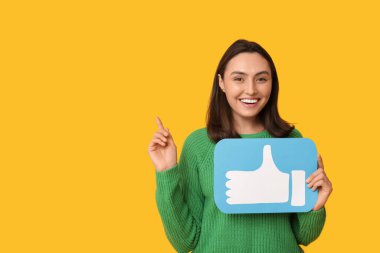 Sarı arka plandaki bir şeyi işaret eden ikon gibi güzel, genç ve mutlu bir kadın.