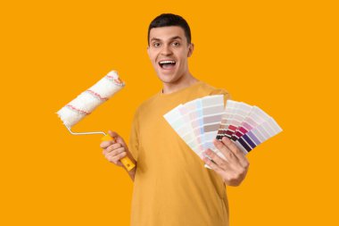 Sarı arka planda renk örnekleri ve boya silindiri olan genç bir adam.