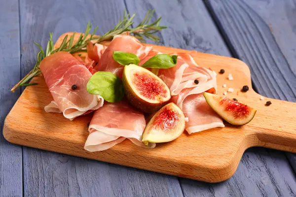 Lezzetli prosciutto, fesleğen ve incir dilimleri mavi ahşap arka planda.