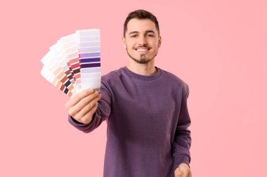 Pembe arka planda boya paletleri olan genç bir adam.