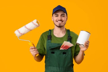 Sarı arka planda boya ve silindirli genç bir ressam.