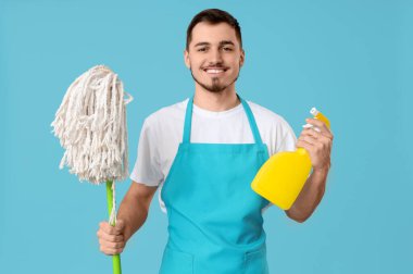 Mavi arka planda temizlik spreyi ve paspası olan erkek hademe.