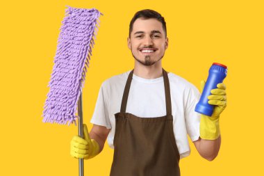 Sarı arka planda temizlik deterjanı ve paspası olan erkek hademe.