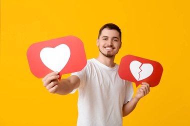 Sarı arka planda ikonları seven ve sevmeyen yakışıklı, mutlu genç bir adam.