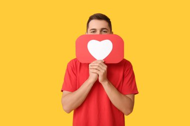 Sarı arkaplanda ikon gibi kalbi olan yakışıklı genç bir adam.