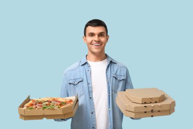 Mutlu genç adam mavi arka planda lezzetli pizzalarla dolu karton kutular tutuyor.