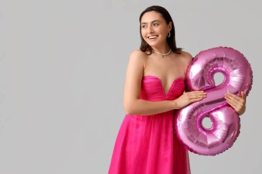 Gri arkaplanda 8 beden şeklinde pembe hava balonu olan güzel genç bir kadın. Uluslararası Kadınlar Günü