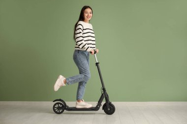 Güzel genç Asyalı kadın yeşil duvarın yanında modern elektrikli scooter kullanıyor.