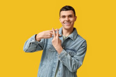 Genç adam sarı arka planda parmaklarıyla hashtag sembolü yapıyor.