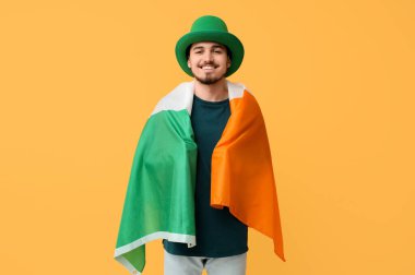 Sarı arka planda İrlanda bayrağı olan cüce şapkalı mutlu genç adam. Aziz Patrick Günü kutlaması