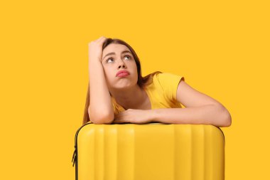 Arka planda sarı bavulu olan üzgün genç kadın.