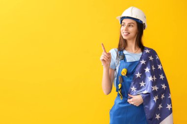 Sarı arka planda ABD bayrağı taşıyan kadın inşaat işçisi.