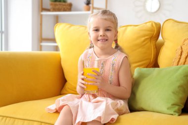 Evdeki kanepede portakal suyu bardağıyla oturan tatlı küçük kız.