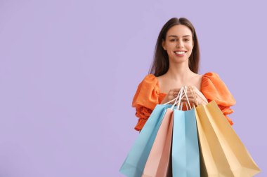Beautiful young woman with shopping bags on lilac background