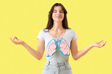 Sarı arka planda meditasyon yapan kağıt ciğerli genç bir kadın.