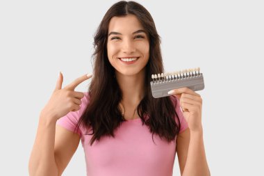 Gülümseyen genç kadın arka planda diş rengine işaret ediyor, yakın plan.