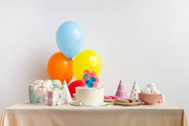 Beyaz duvara karşı pasta, şeker ve doğum günü partisi için dekorasyon masası.