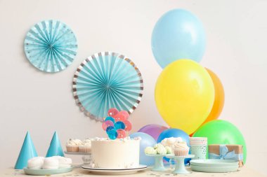 Beyaz duvara karşı pasta, şeker ve doğum günü partisi için dekorasyon masası.